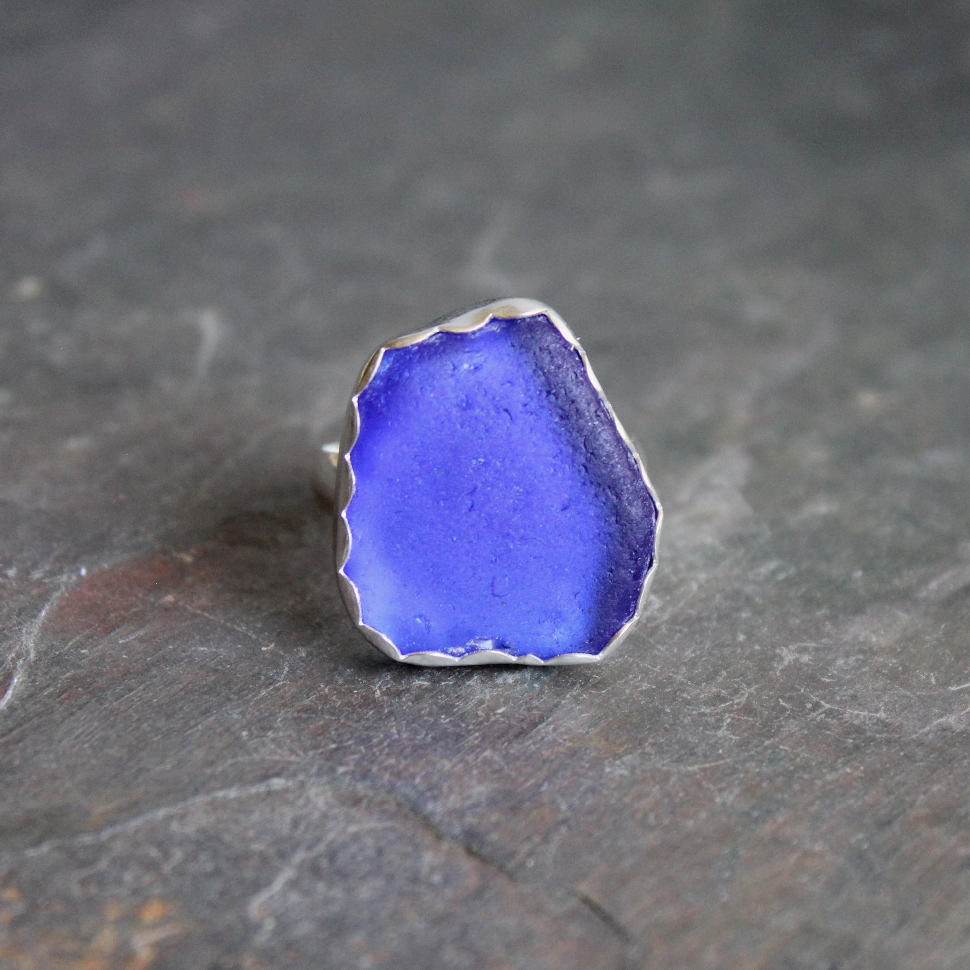 Blue sea glass ring with silver setting on a dark stone surface