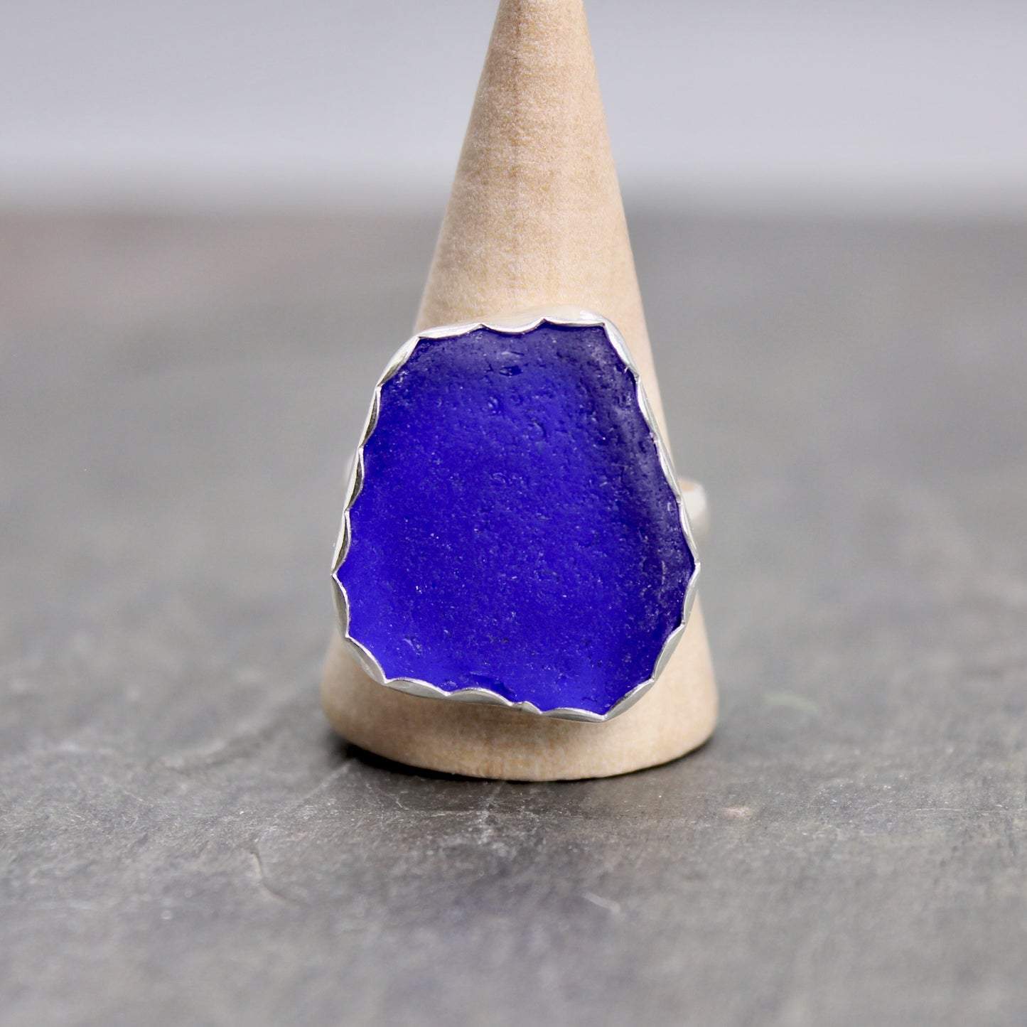 Blue sea glass ring on a wooden stand against a gray background