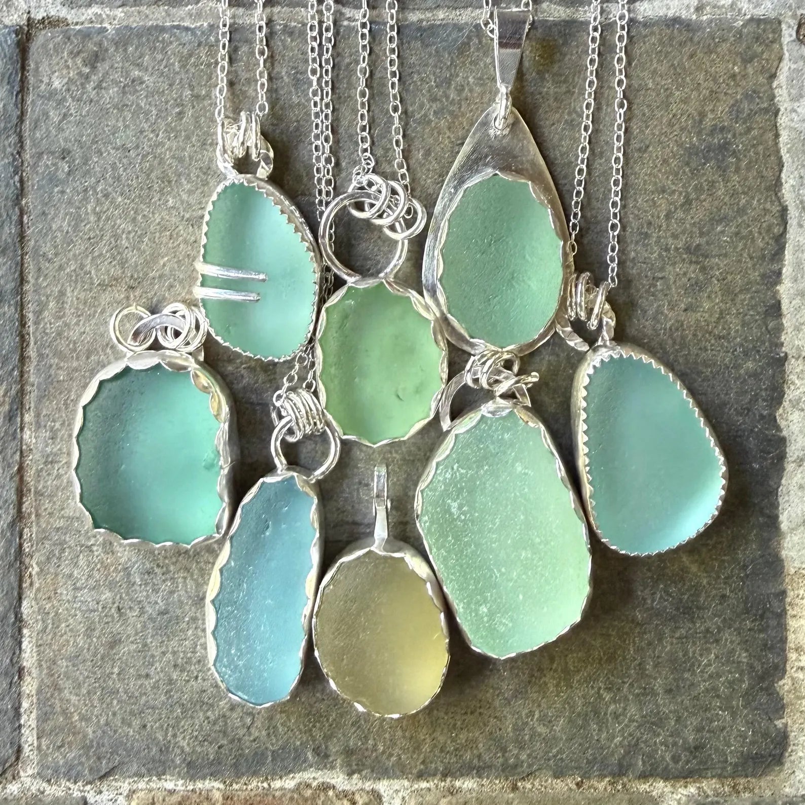Green and silver sea glass pendant necklaces on a stone surface