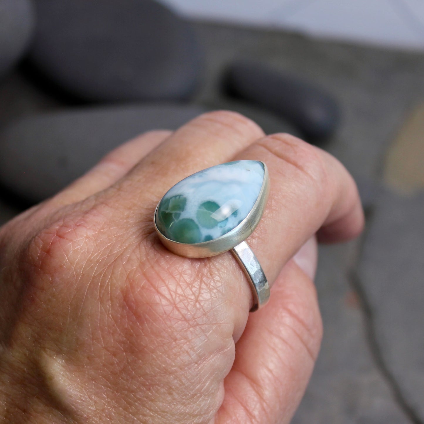 Hand wearing a silver ring with a green stone against a blurred natural background