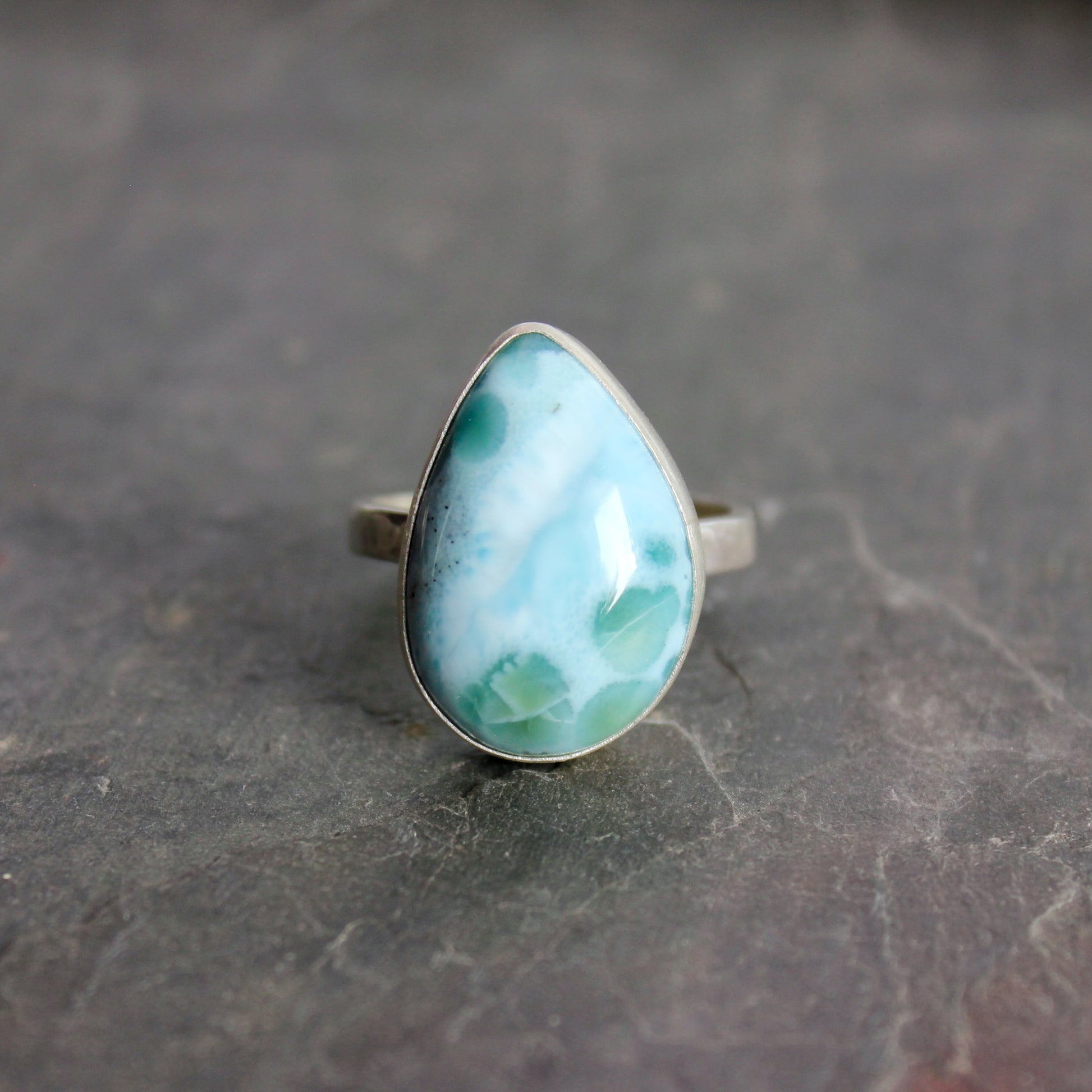 Teardrop-shaped larimar ring on a gray surface