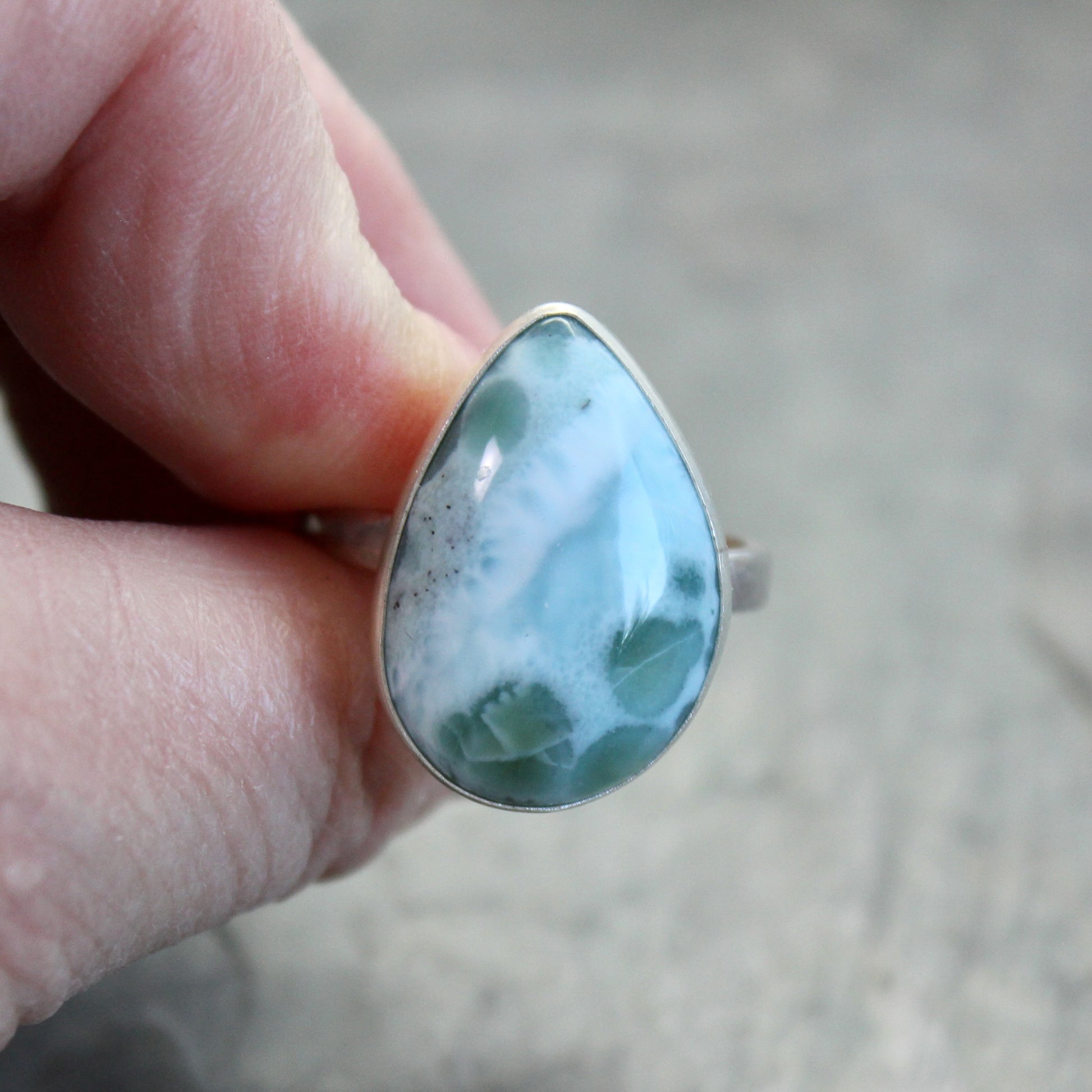 Teardrop-shaped larimar ring on a gray surface
