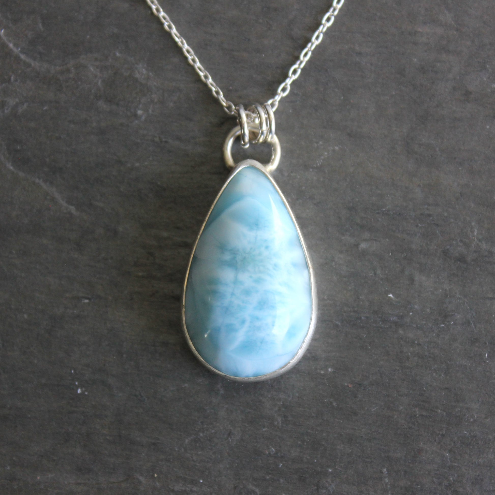 Teardrop-shaped blue larimar pendant on a silver chain against a dark background