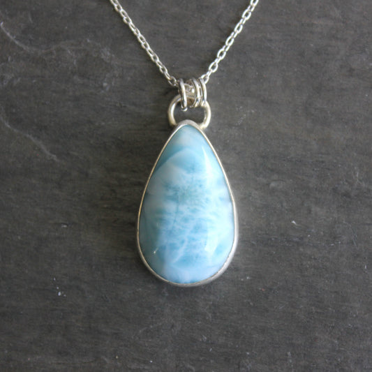 Teardrop-shaped blue larimar pendant on a silver chain against a dark background