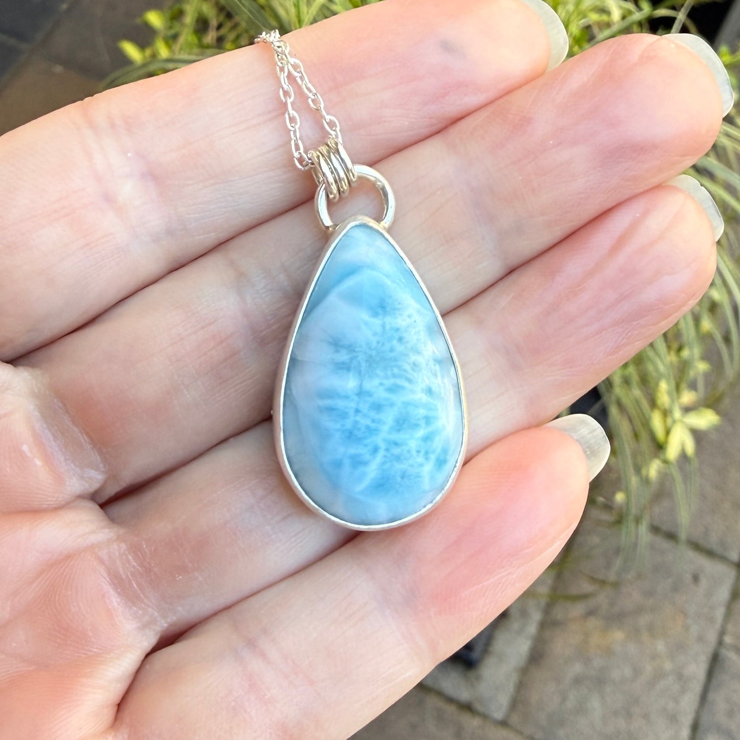 Teardrop-shaped blue larimar pendant on a silver chain on a hand