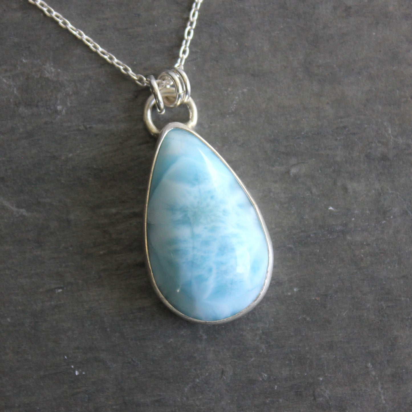 Teardrop-shaped blue larimar pendant on a silver chain against a dark background
