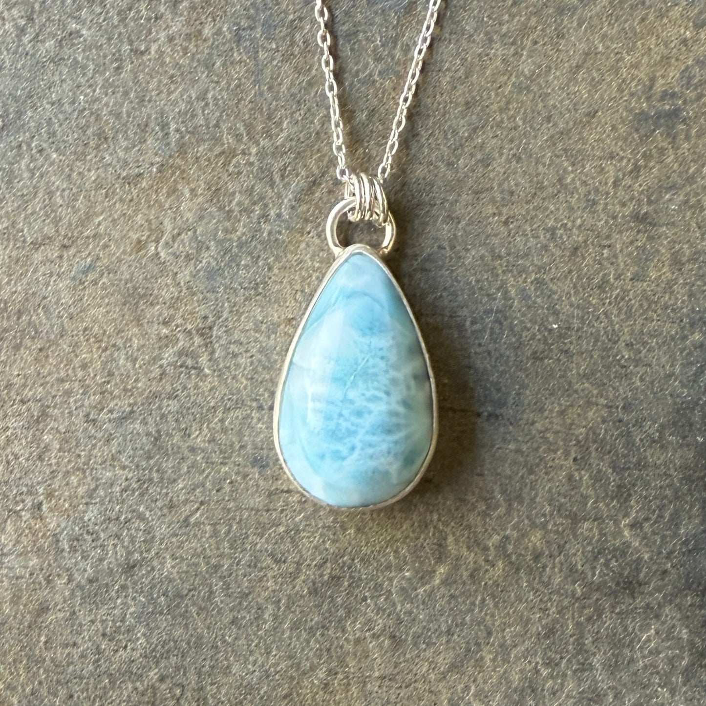 Teardrop-shaped blue larimar pendant on a silver chain against a dark background