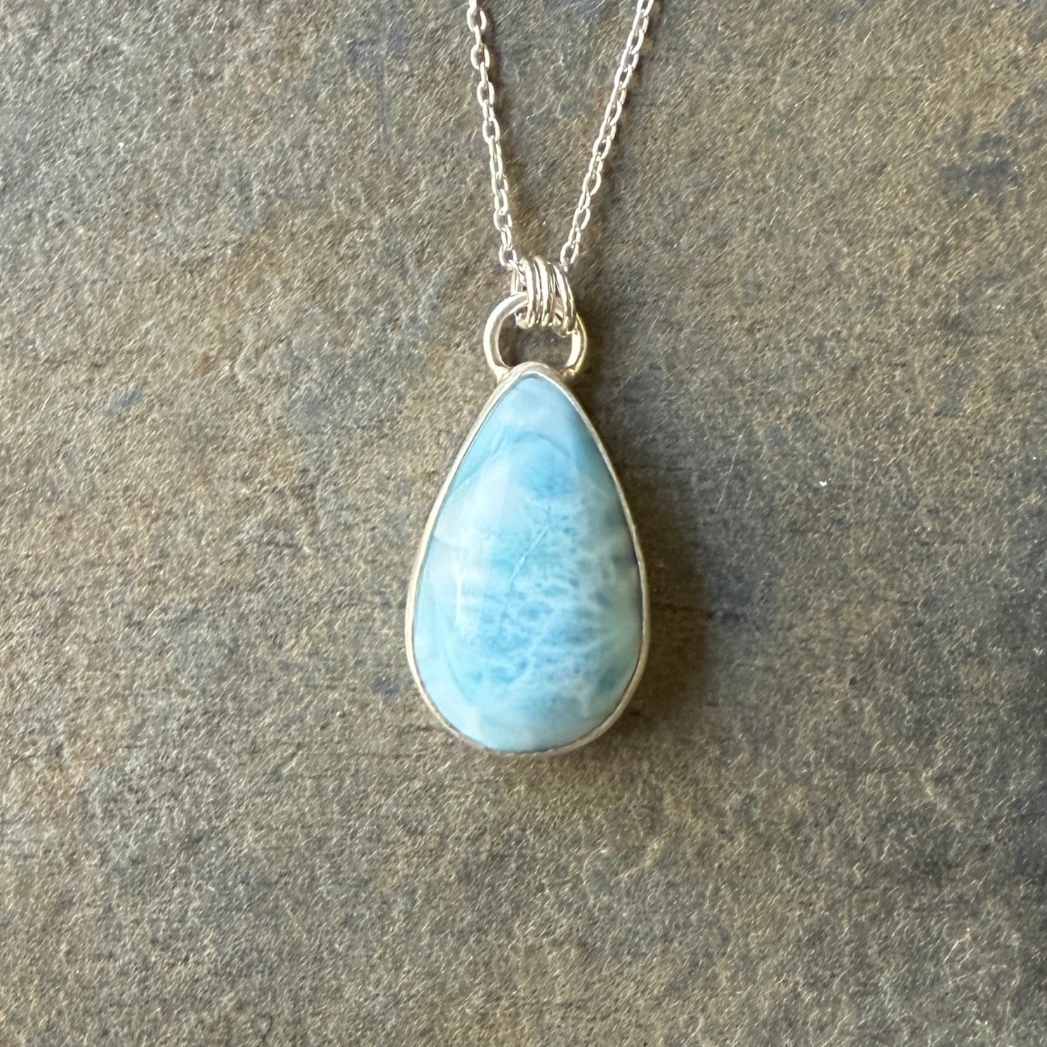 Teardrop-shaped blue larimar pendant on a silver chain against a dark background