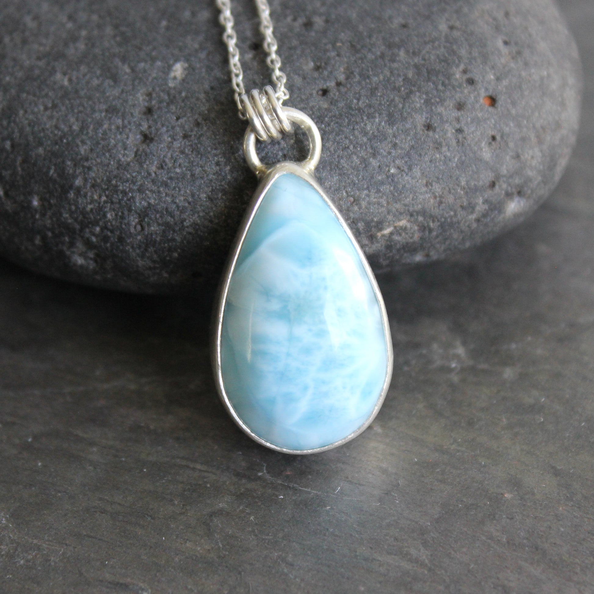 Teardrop-shaped blue larimar pendant on a silver chain against a dark background