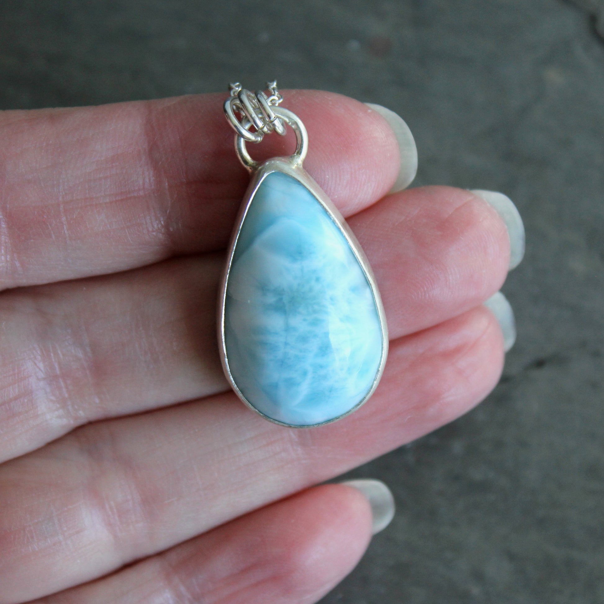 Teardrop-shaped blue larimar pendant on a silver chain against a dark background