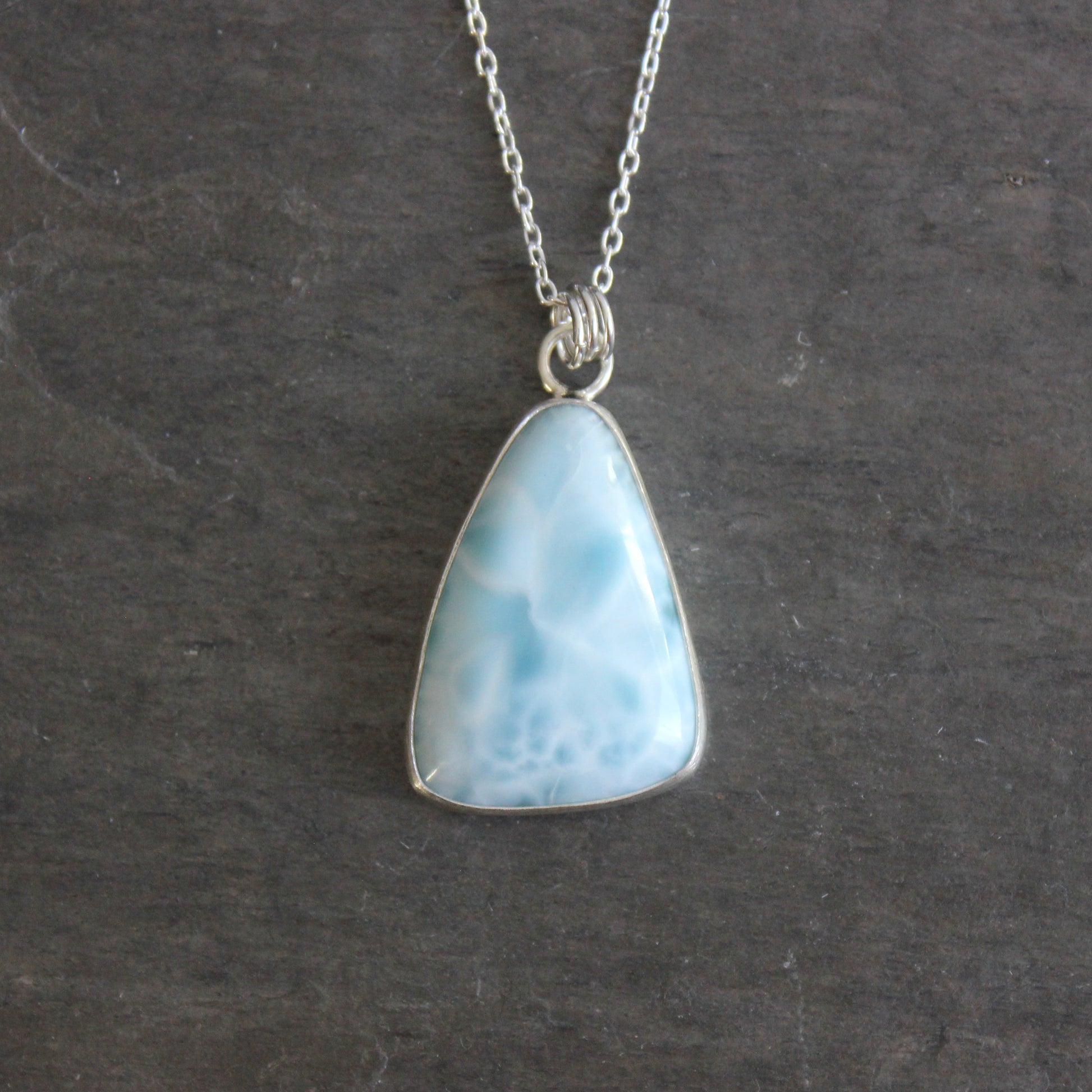 Necklace with a triangular blue larimar pendant on a dark gray background