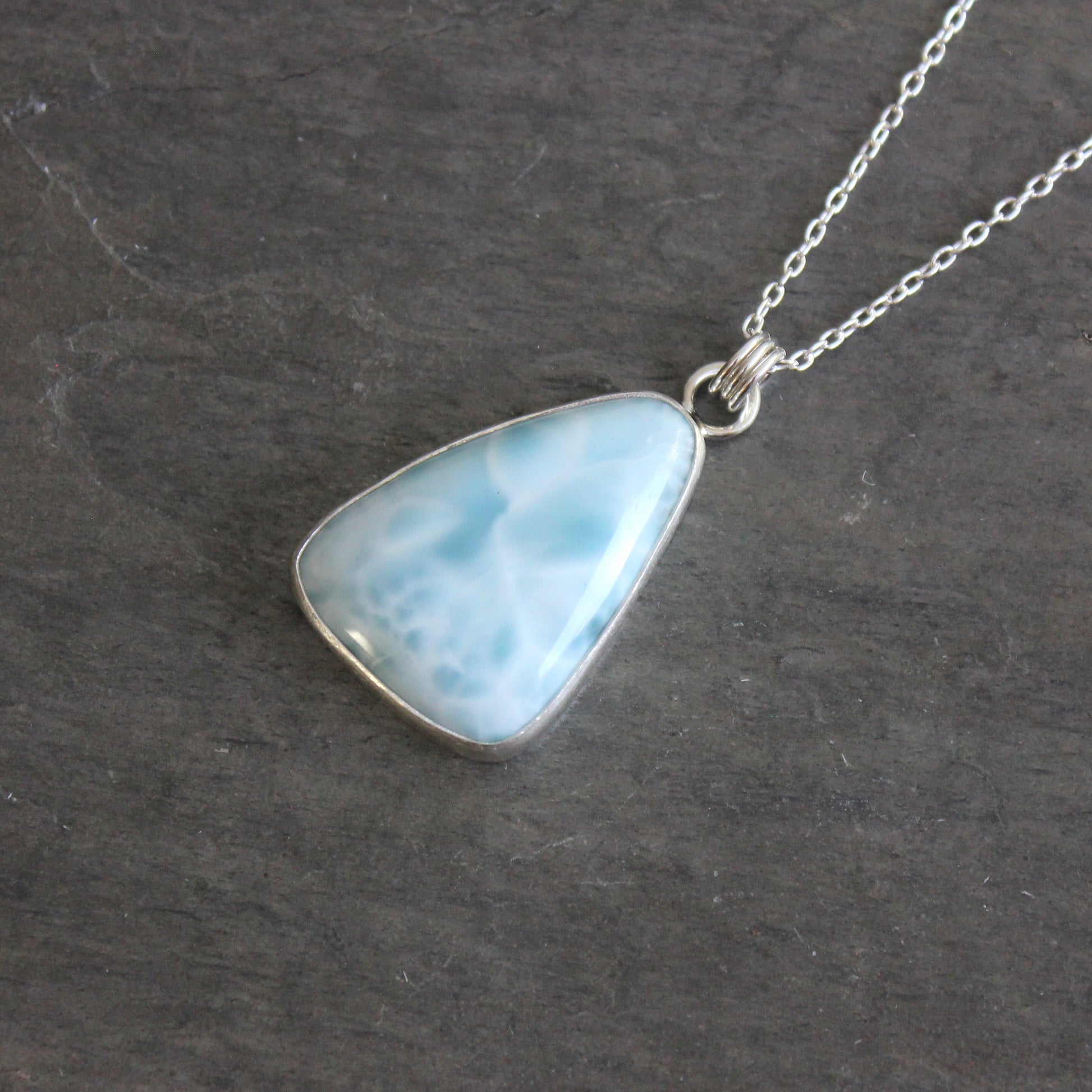 Necklace with a triangular blue larimar pendant on a dark gray background