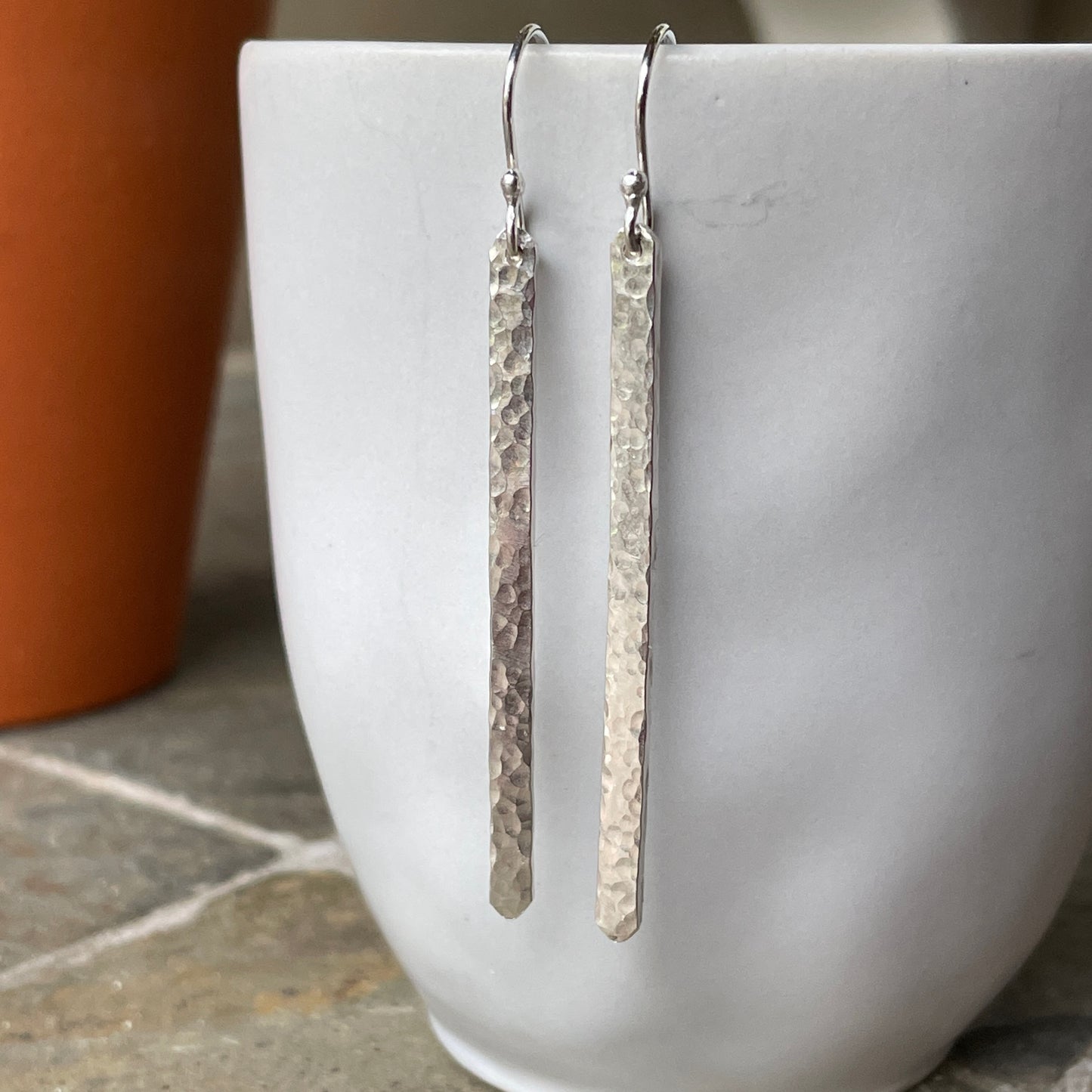Silver earrings hanging from a white cup on a stone surface