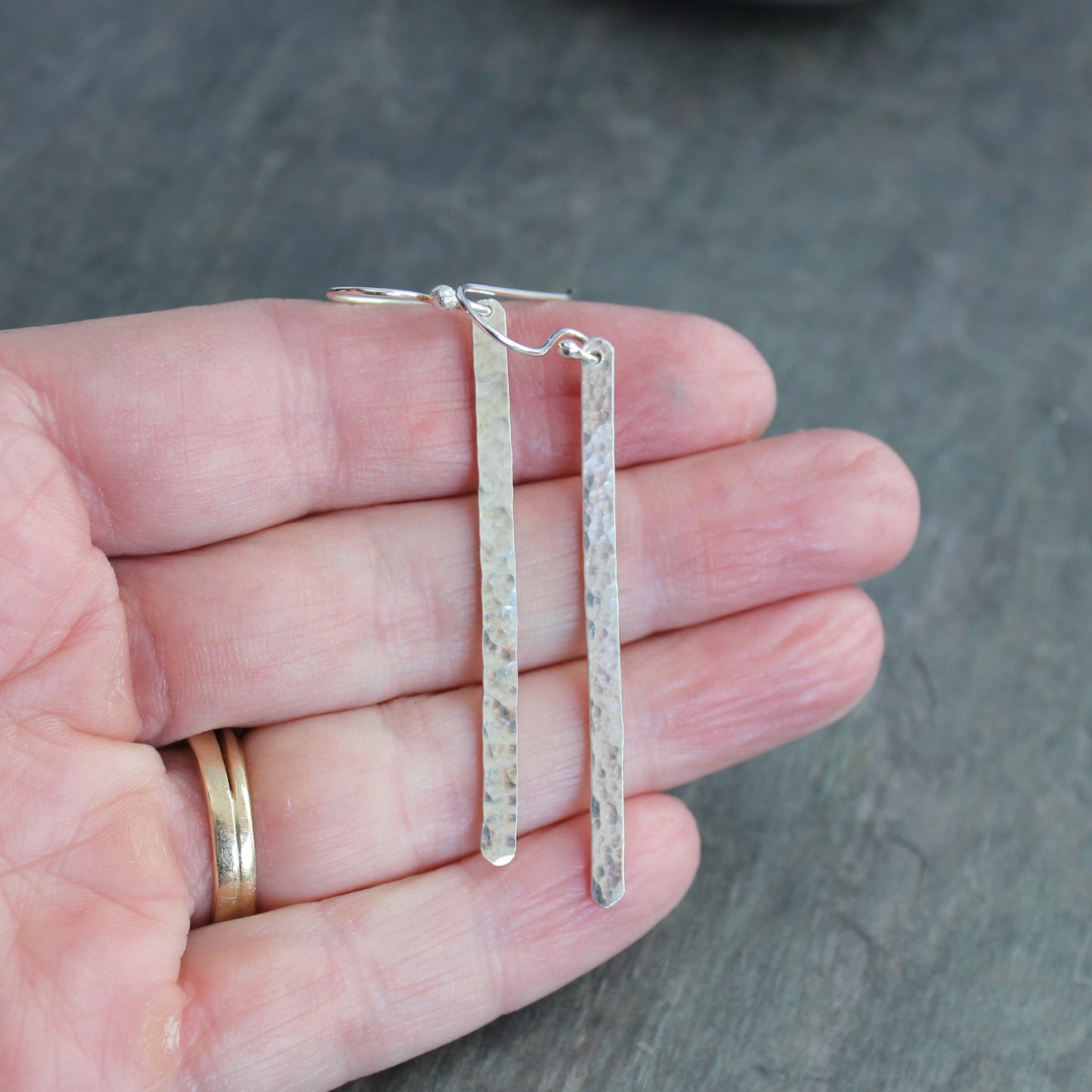 Silver earrings held in a hand against a gray background