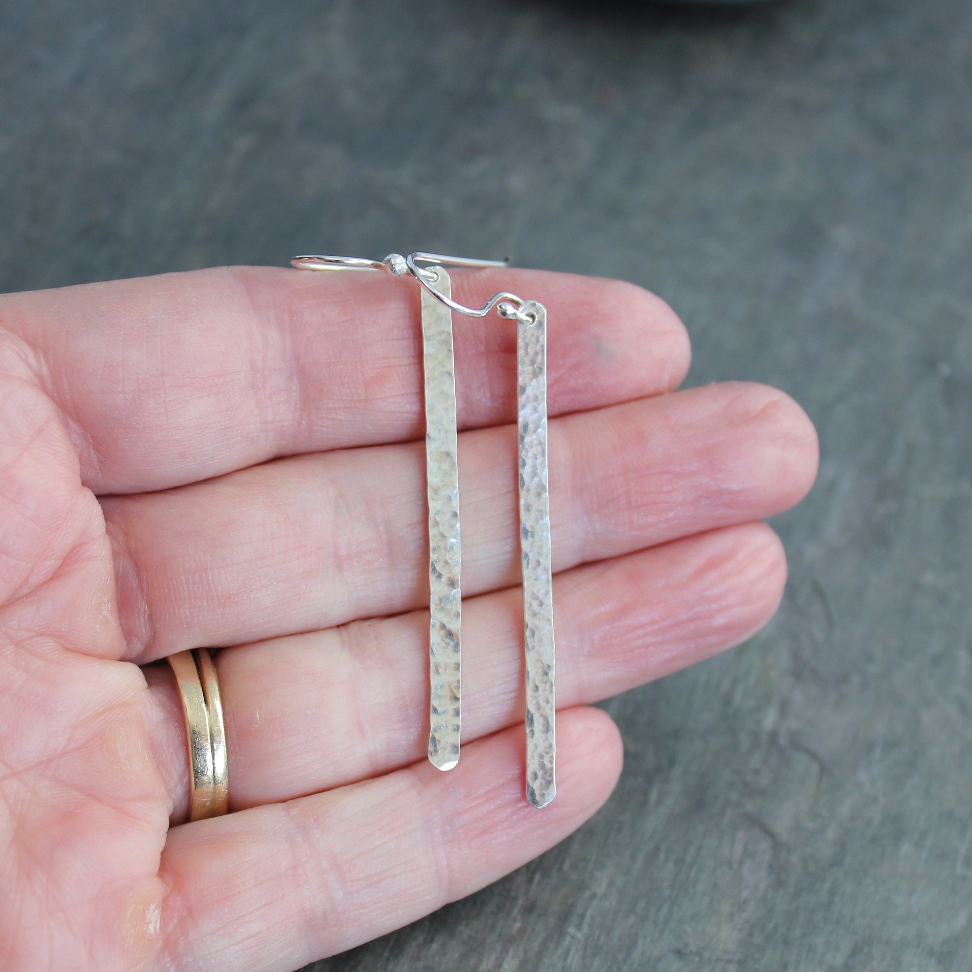 Silver earrings held in a hand against a gray background