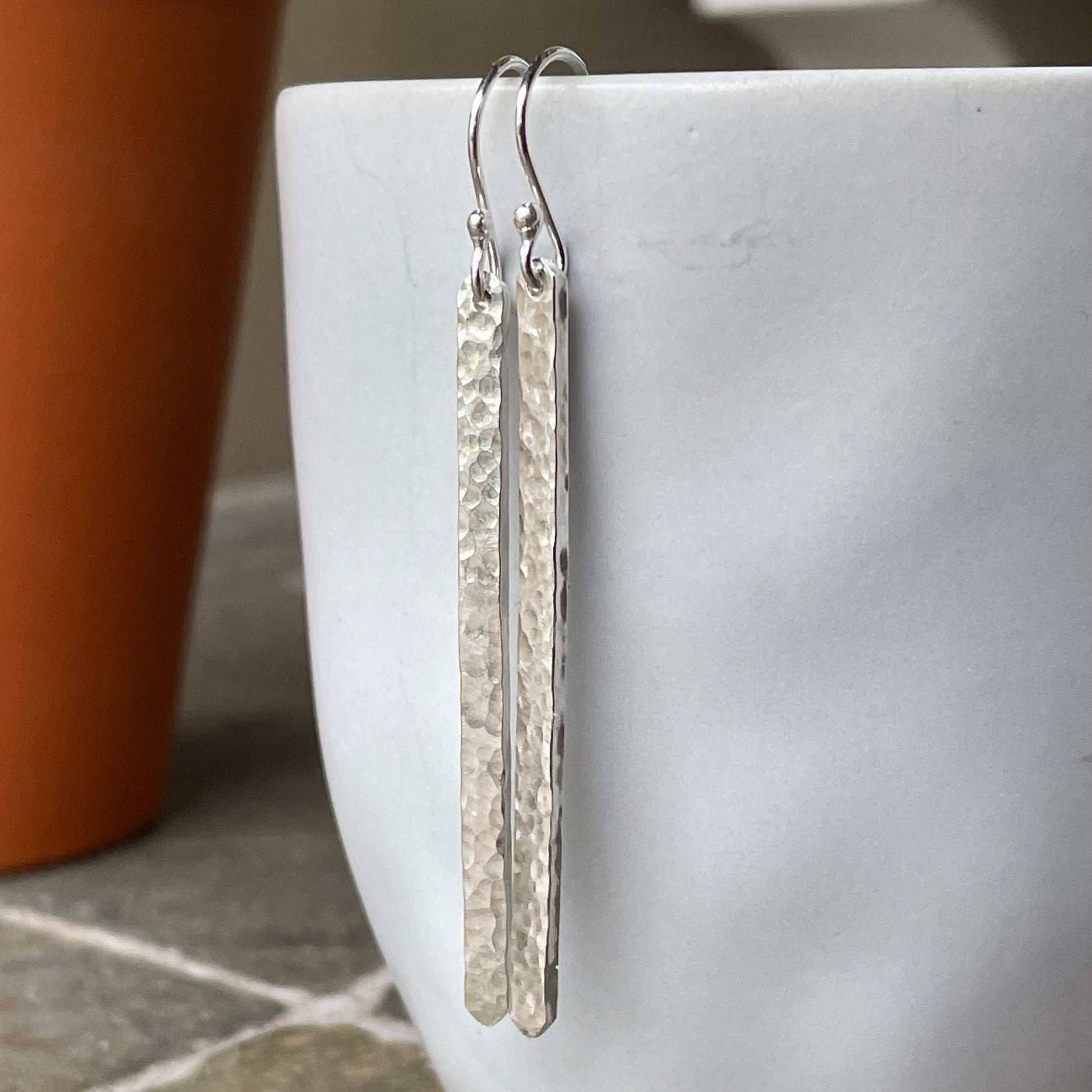 Silver earrings hanging from a white cup with a blurred background