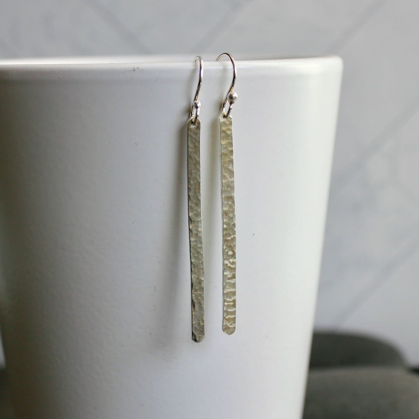 Pair of silver earrings hanging on a white surface with a blurred background