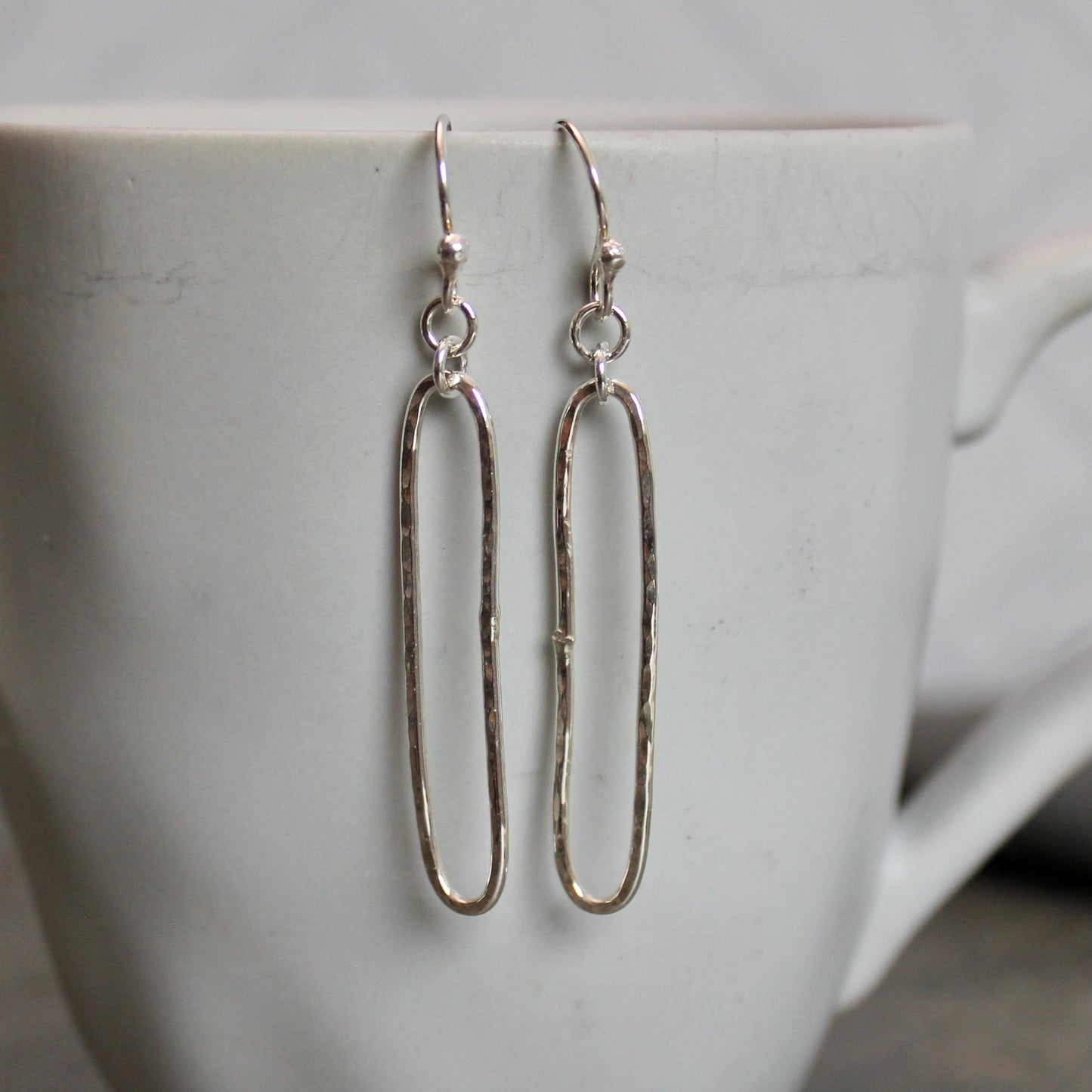 Pair of sterling silver oval earrings on a white cup