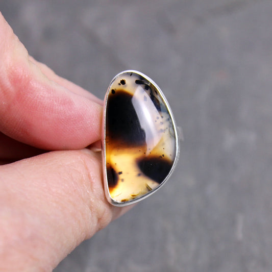 Hand holding a ring with a montana agate stone against a blurred background