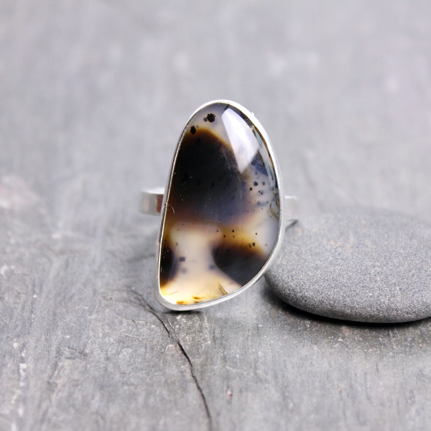 Silver ring with a large, multicolored stone on a gray stone surface