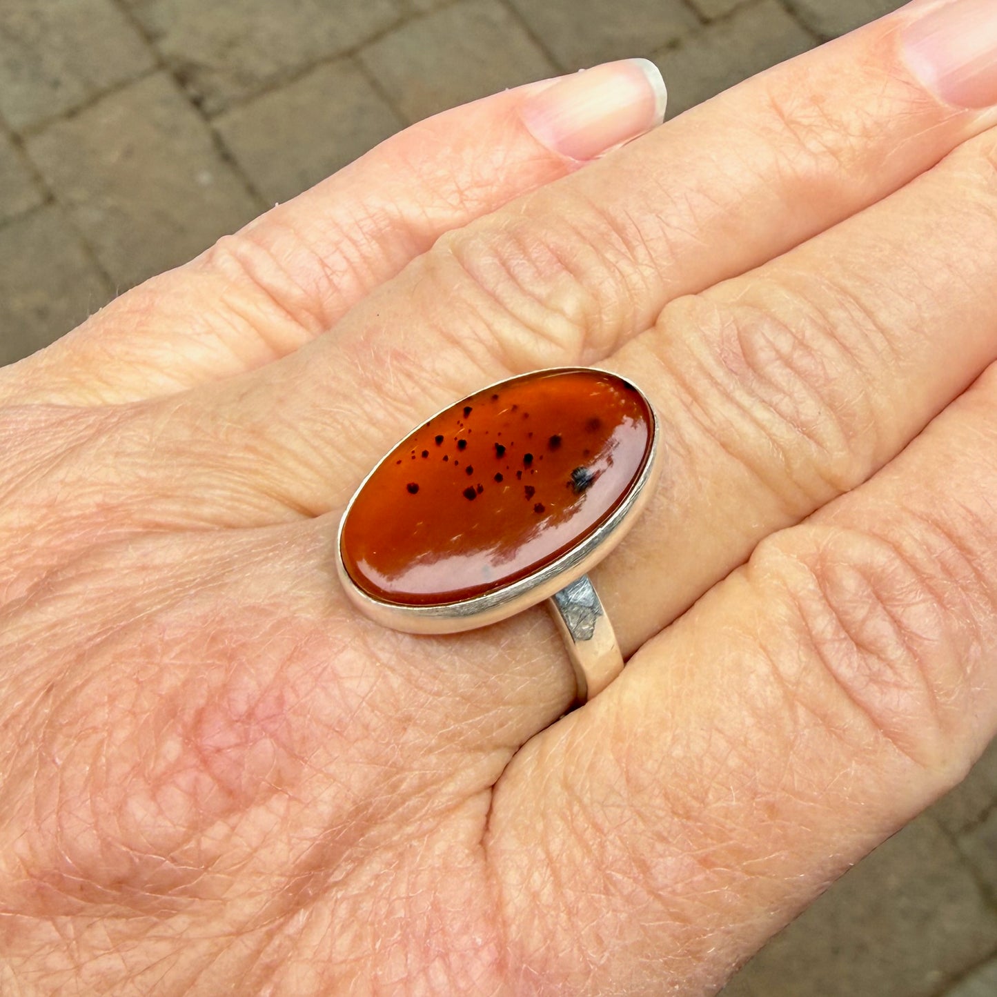 Hand wearing a ring with an Orange Montana Agates on a brick pavement background