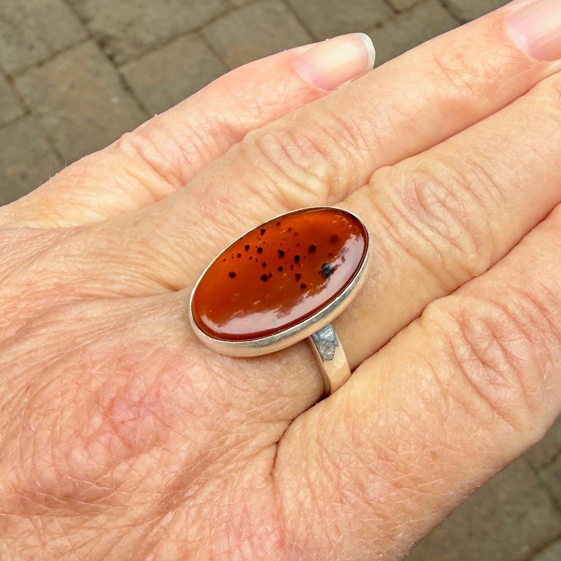 Hand wearing a ring with an Orange Montana Agates on a brick pavement background