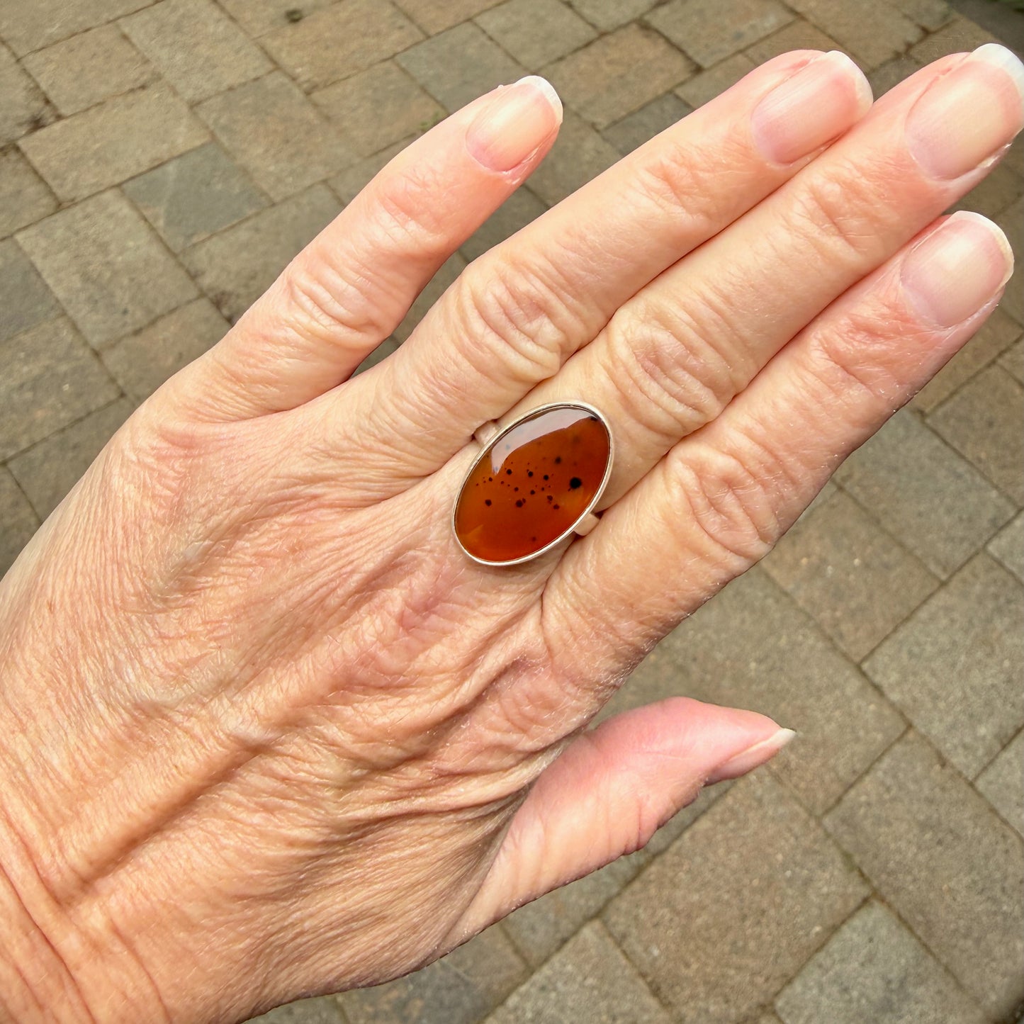 Hand wearing a ring with an Orange Montana Agates on a brick pavement background