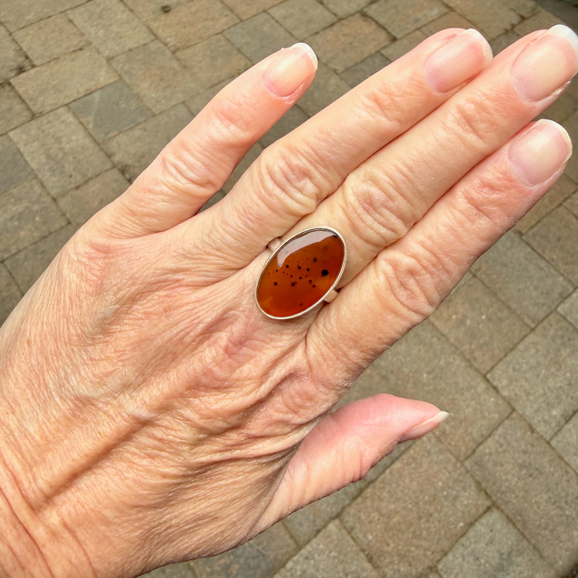 Hand wearing a ring with an Orange Montana Agates on a brick pavement background