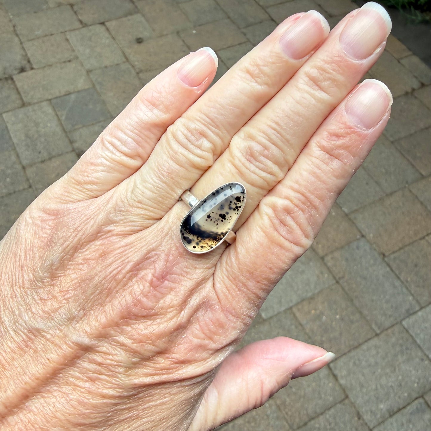 Hand wearing a ring with a Spotted Montana Agate on a paved surface