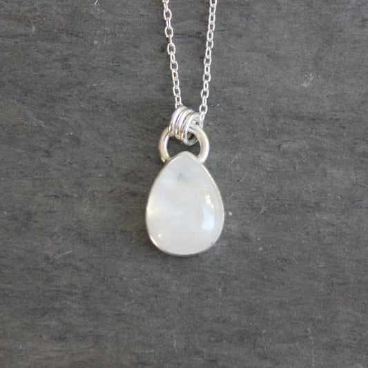 Teardrop-shaped pendant on a chain against a gray background