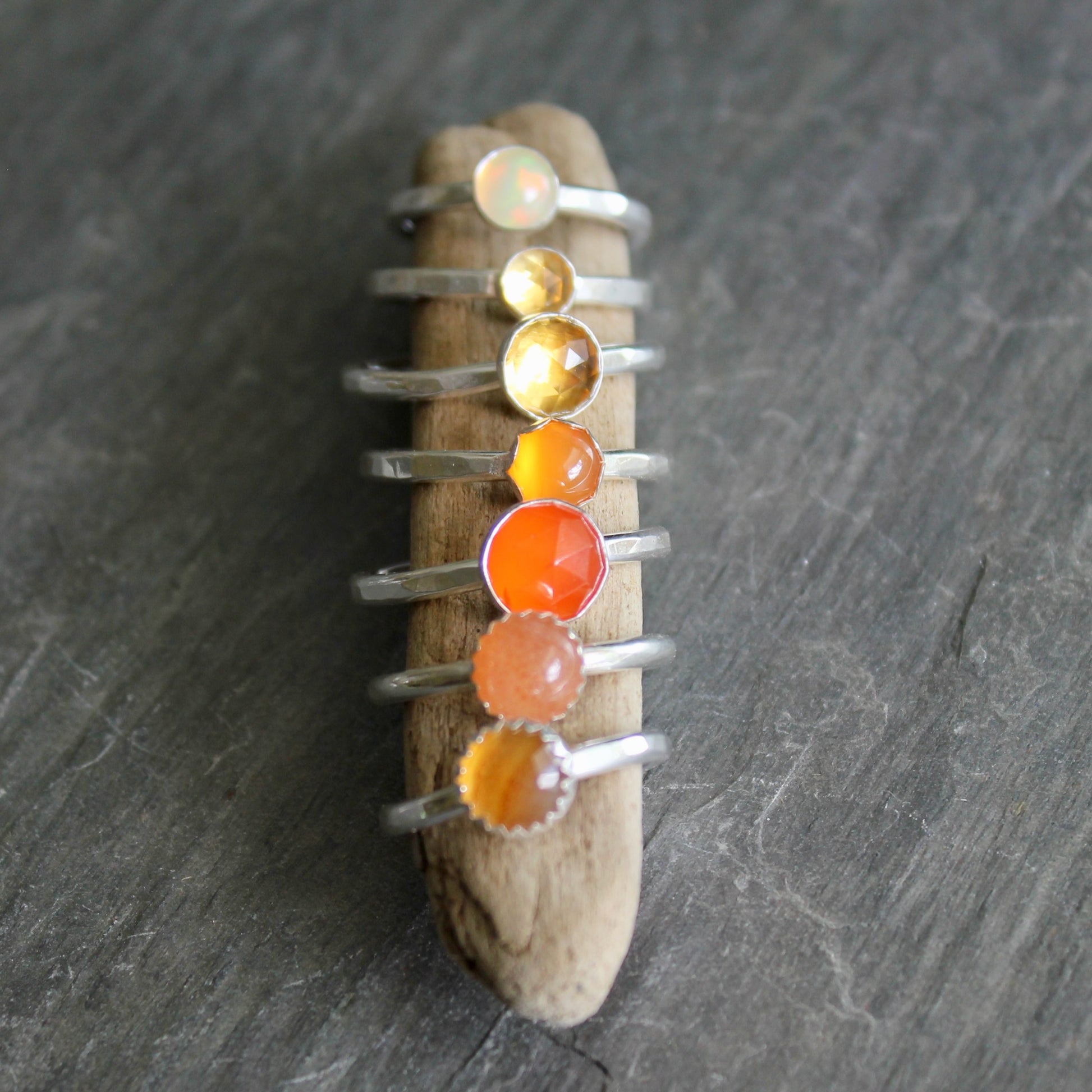 Set of silver rings with orange gemstones on a piece of driftwood against a dark background