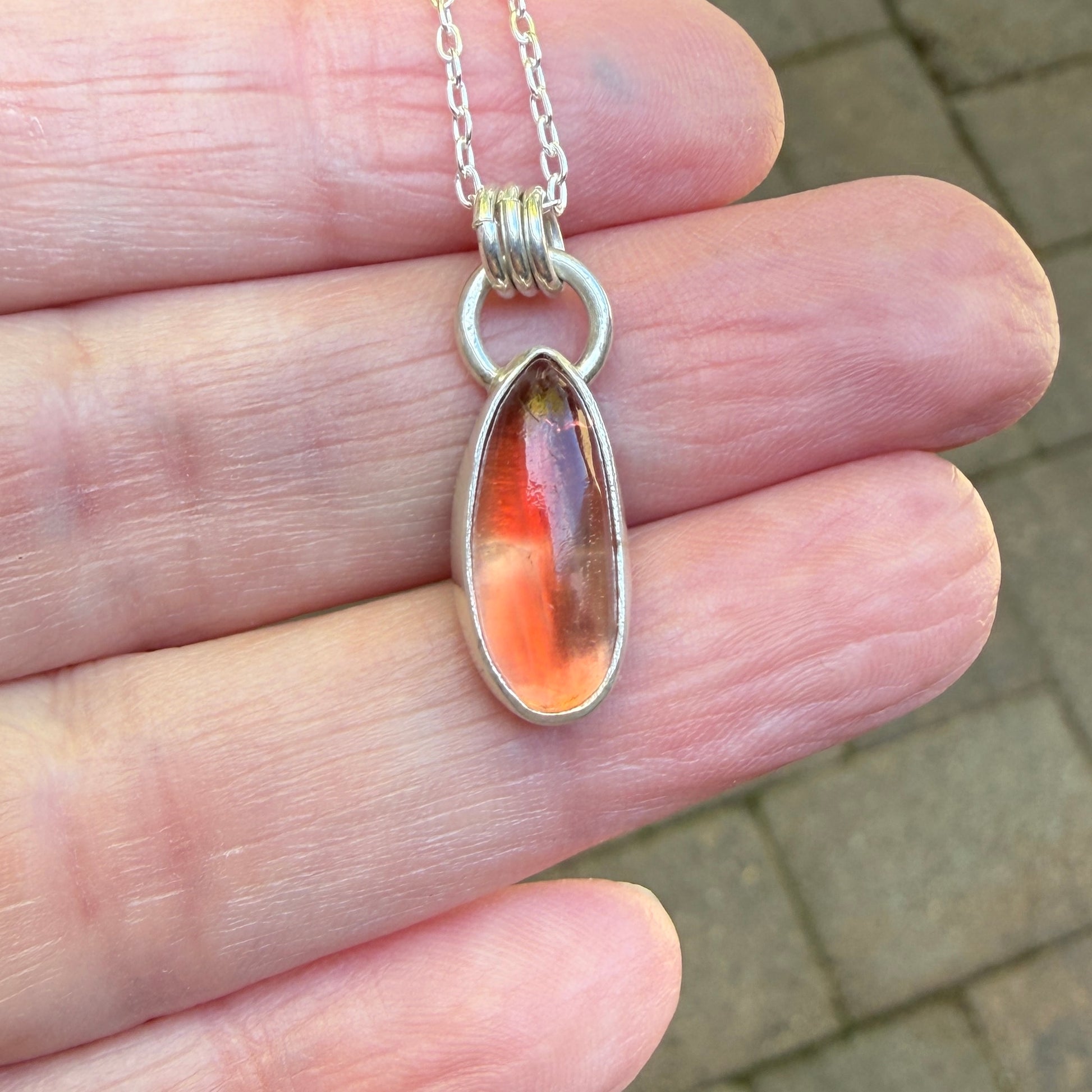 Silver pendant with a teardrop-shaped oregon sunstone held between fingers.