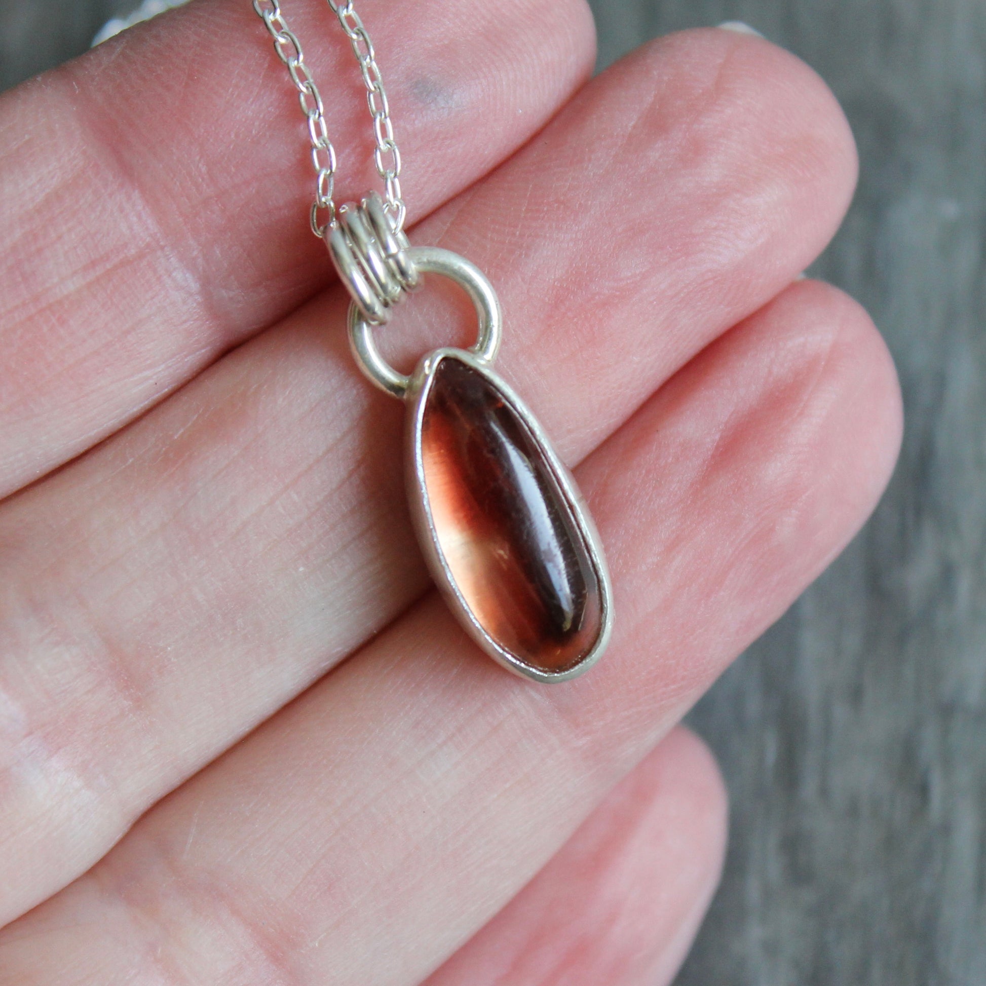 Necklace with a pendant featuring a oregon sunstone held in a hand against a neutral background