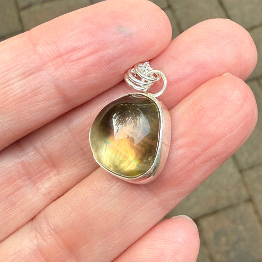 Silver pendant with a greenish oregon sunstone held between fingers on a blurred background