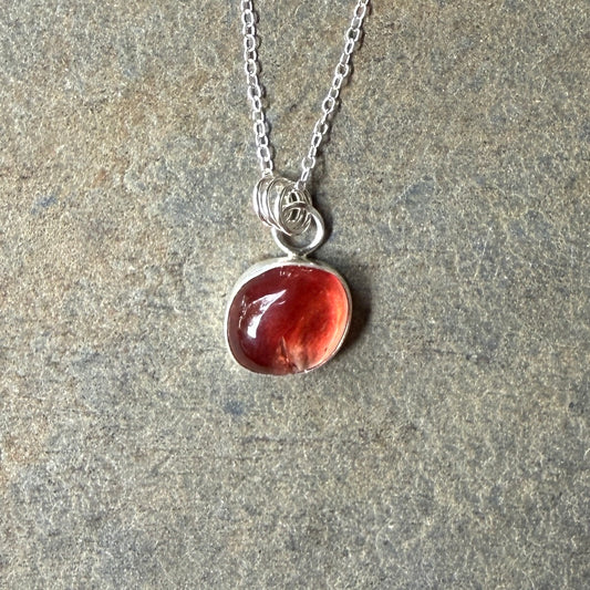 Necklace with a red oregon sunstone pendant on a stone surface