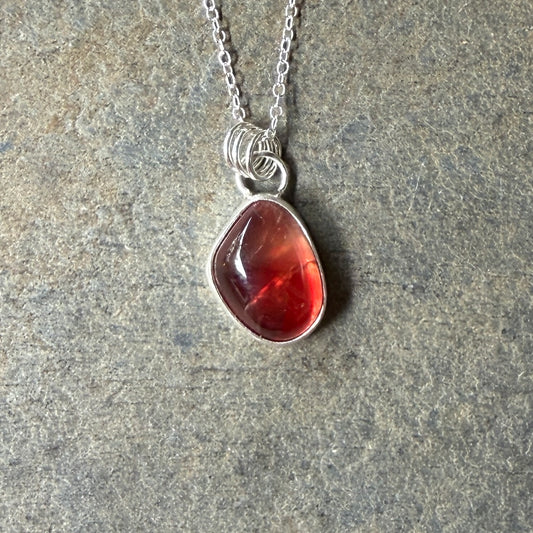 Necklace with a red oregon sunstone pendant on a gray stone surface