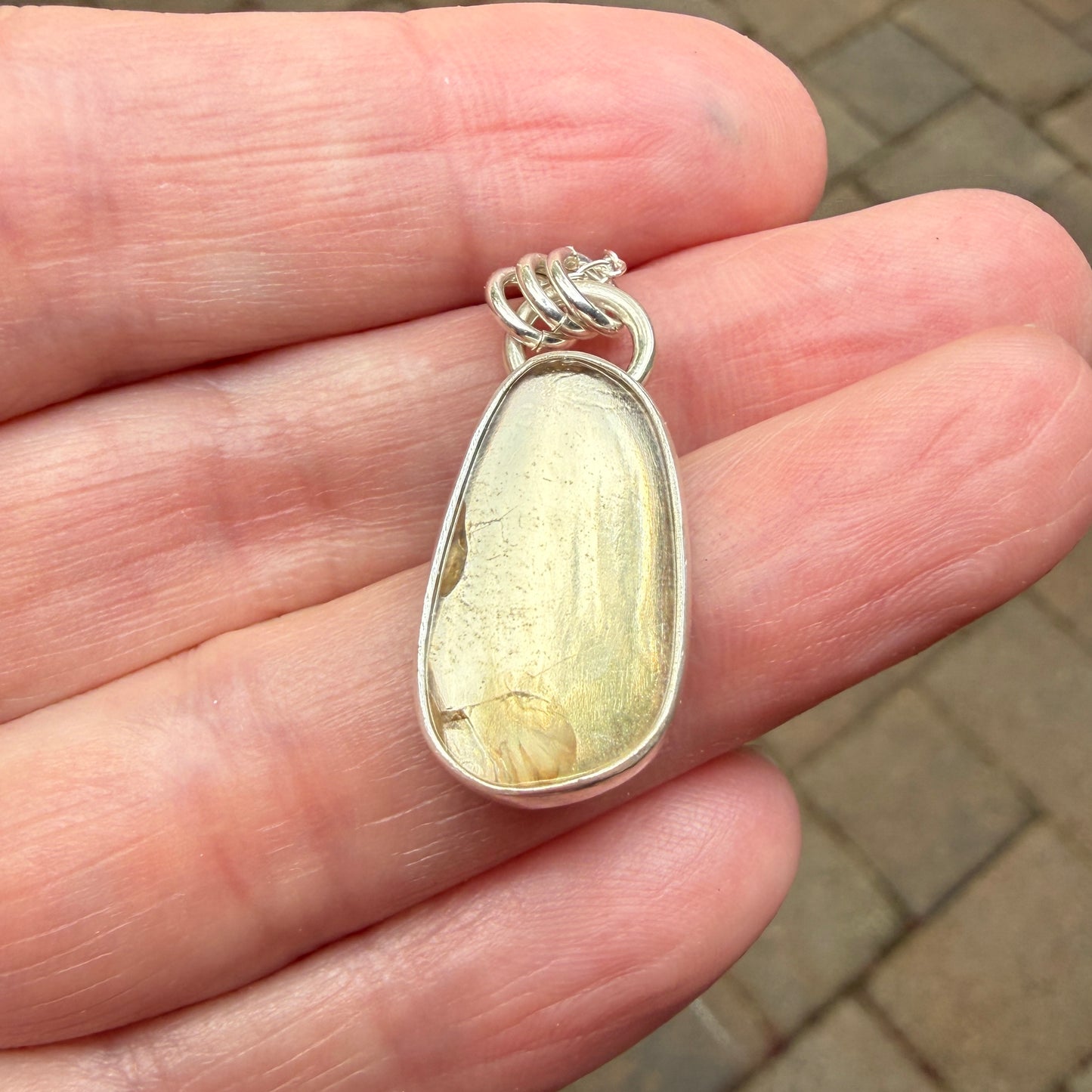 Silver pendant with a yellow stone held in a hand on a blurred background