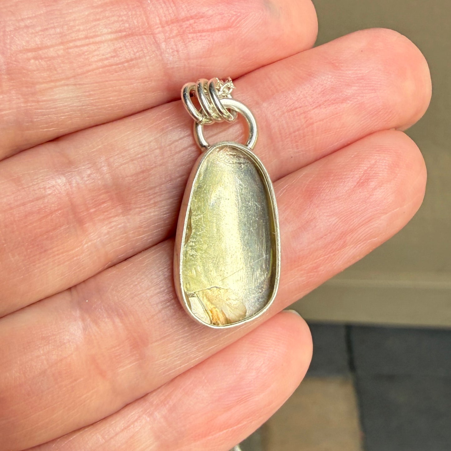 Silver pendant with a yellowish stone held in a hand