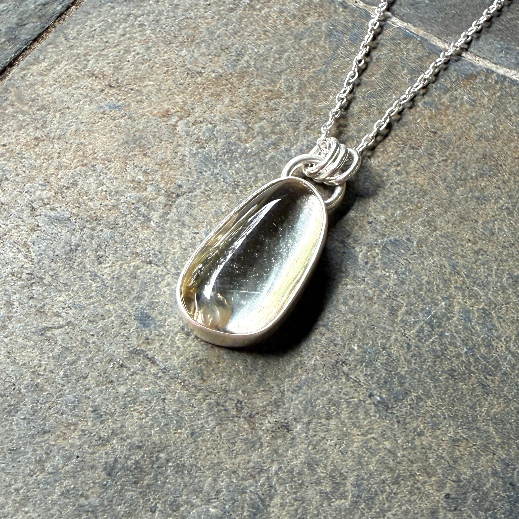 Silver pendant necklace with a champagne clear sunstone on a stone surface