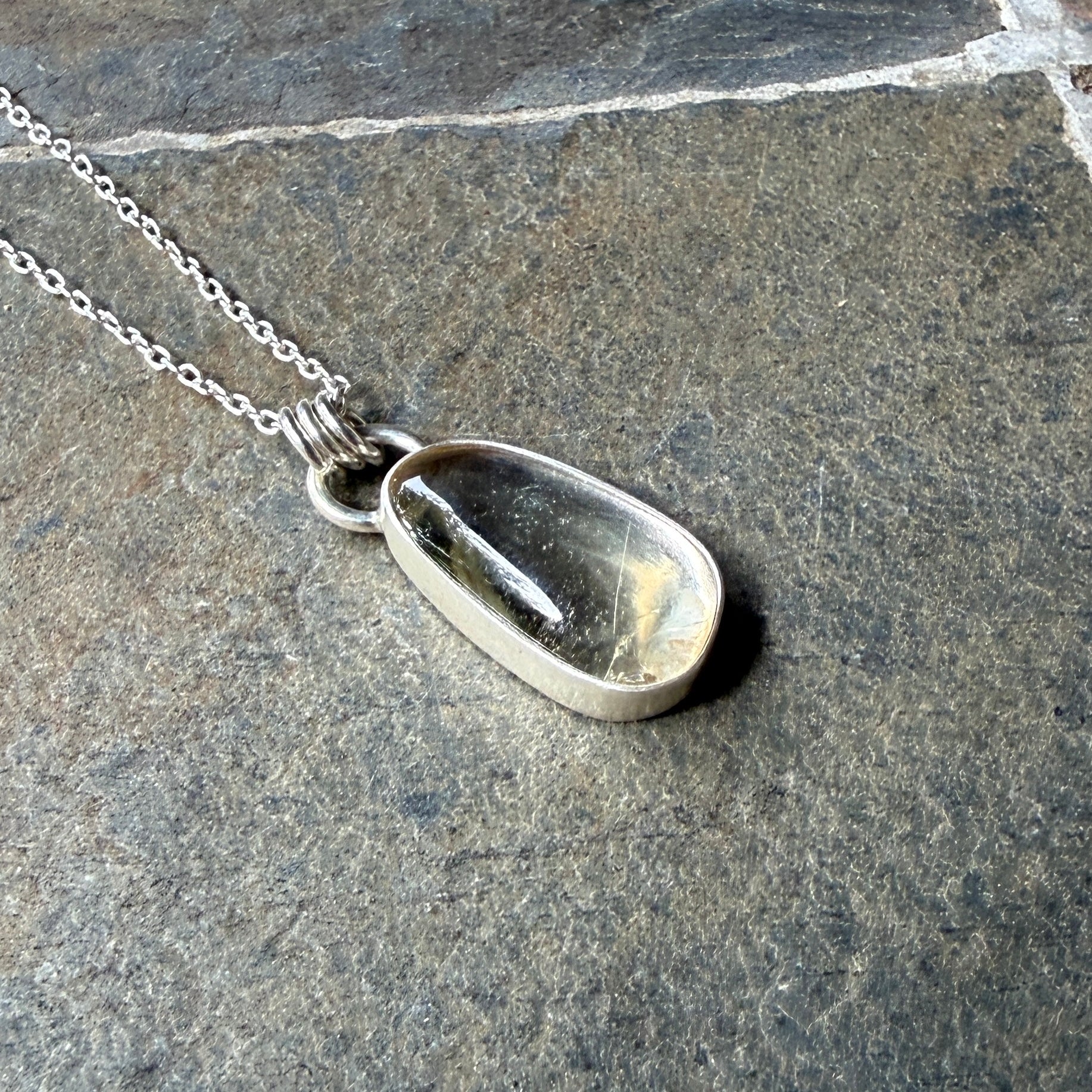 Silver pendant necklace with a champagne clear sunstone on a stone surface