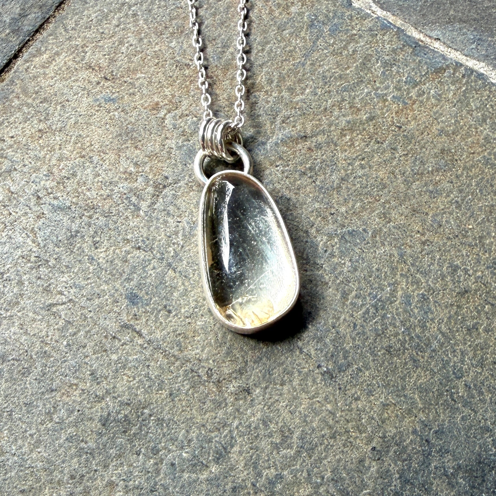 Silver pendant necklace with a champagne clear sunstone on a stone surface