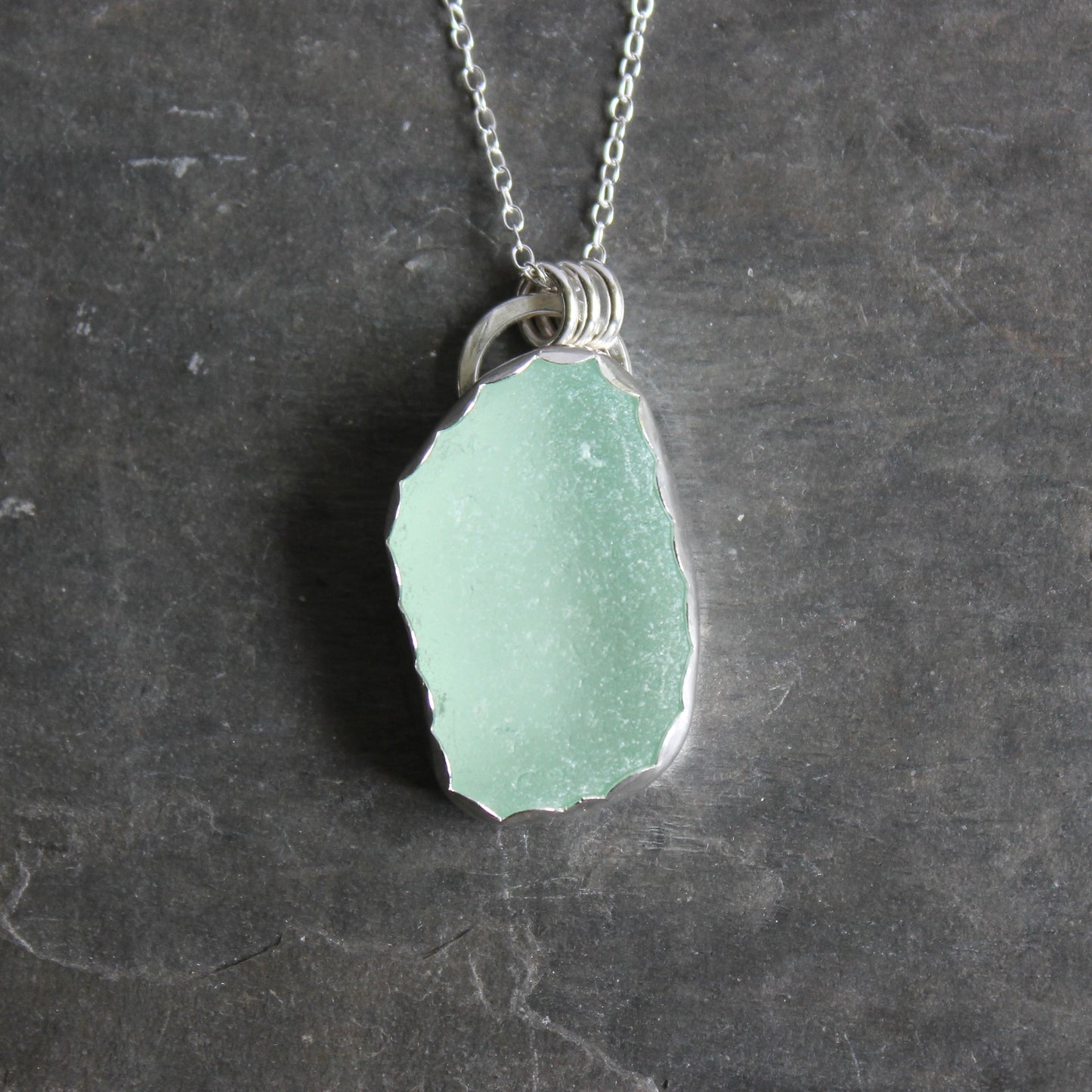 Green sea glass pendant on a silver chain against a dark stone background