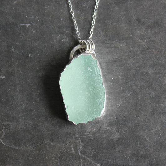 Green sea glass pendant on a silver chain against a dark stone background