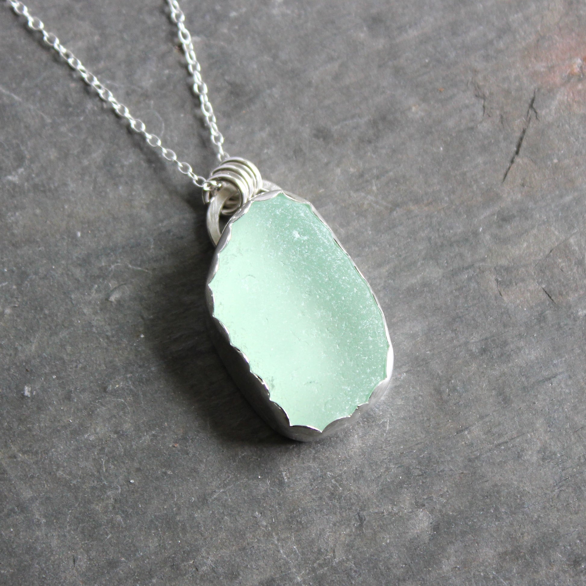 Necklace with a light green sea glass pendant on a dark gray surface
