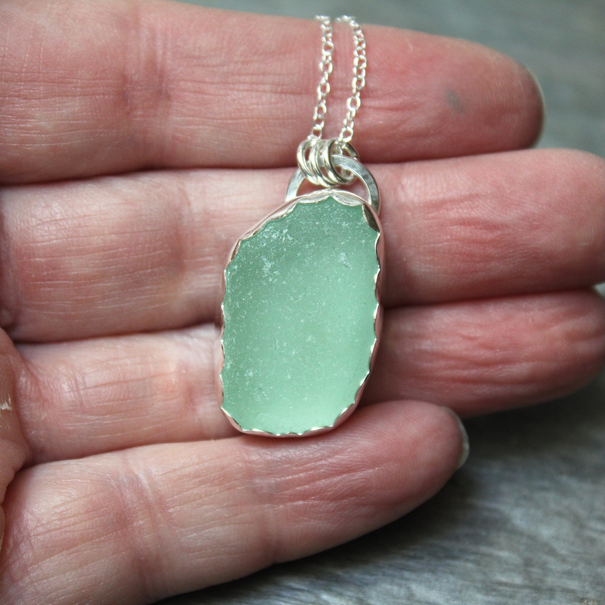 Green sea glass pendant necklace held in a hand against a neutral background