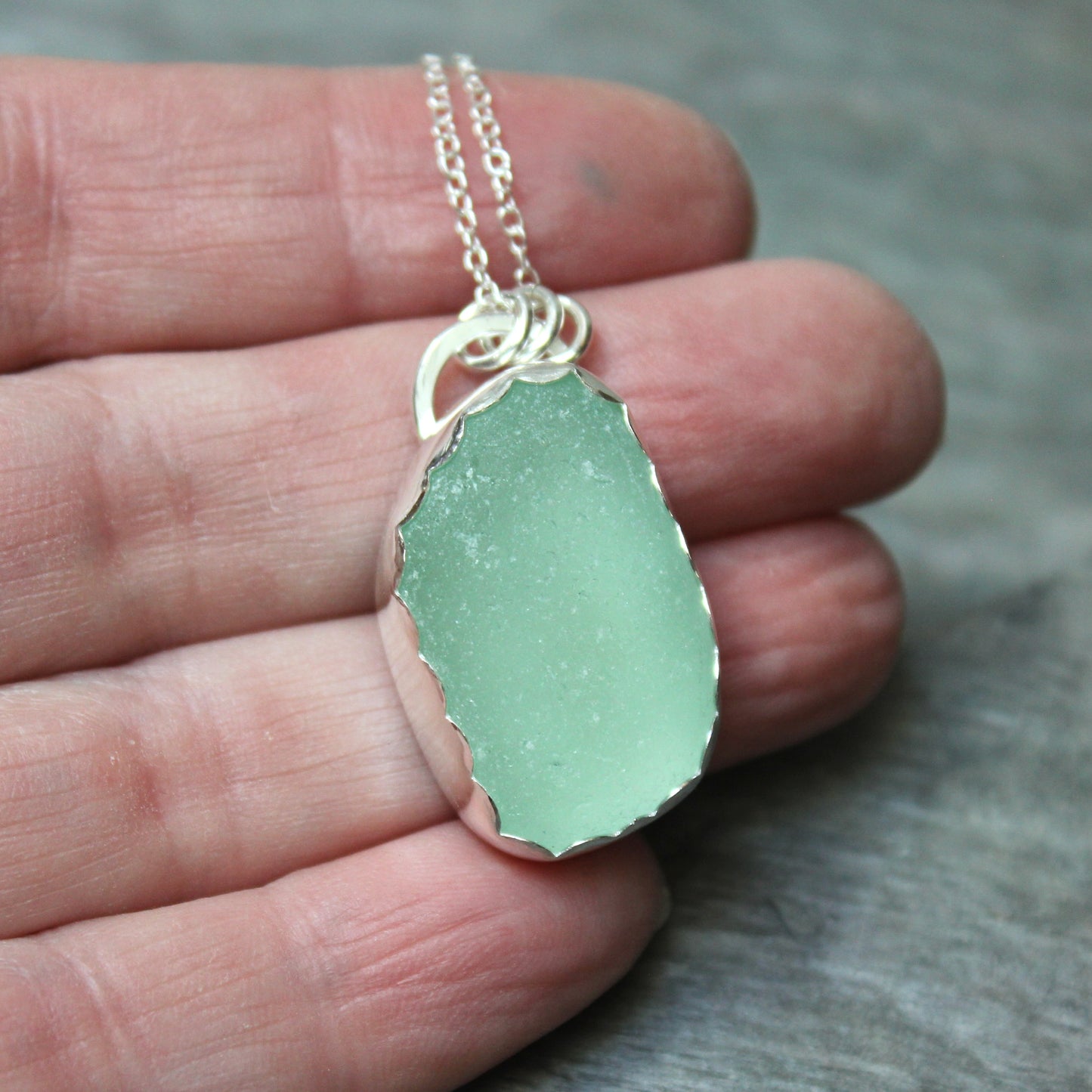 Green pendant necklace held in a hand against a neutral background