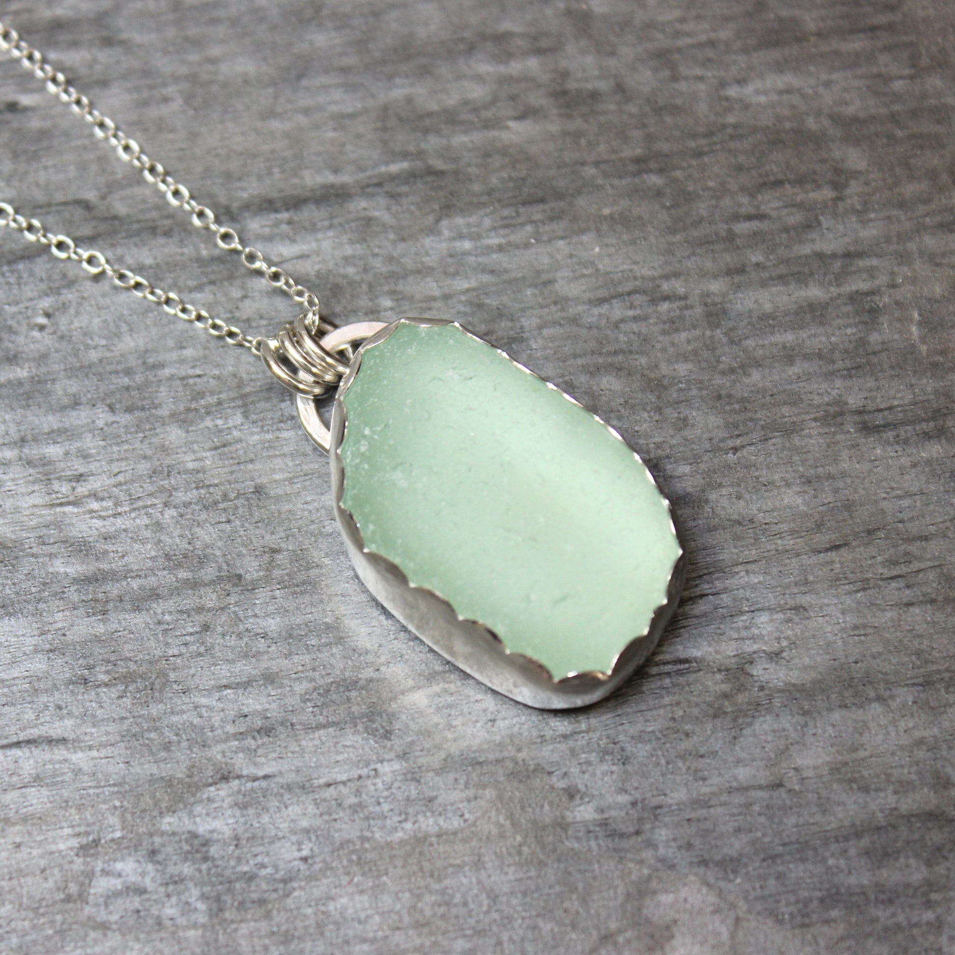 Necklace with a light green sea glass pendant on a wooden surface