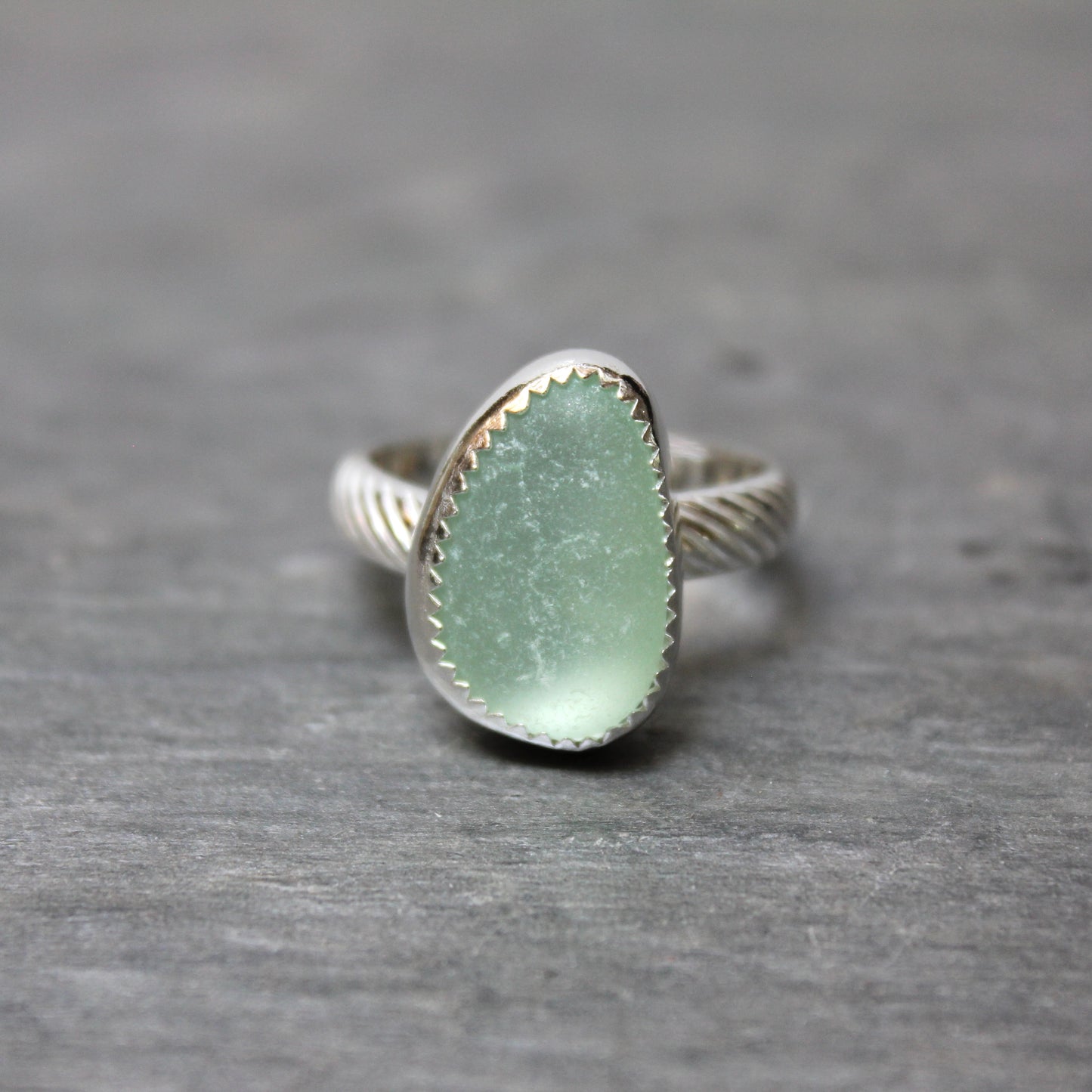 Ring with a green sea glass and silver band on a gray background