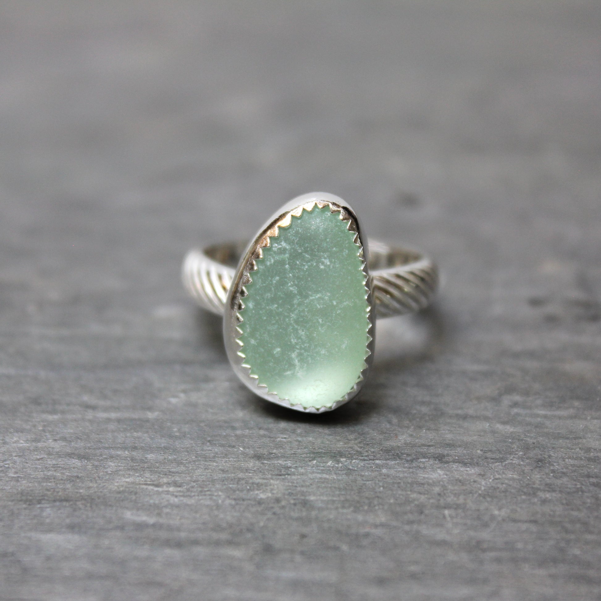 Ring with a green sea glass and silver band on a gray background