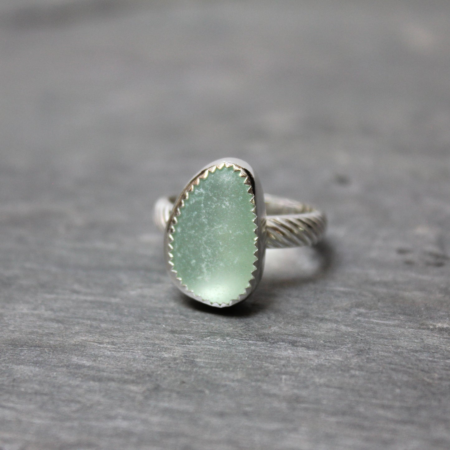 Green sea glass ring with silver band on a gray surface